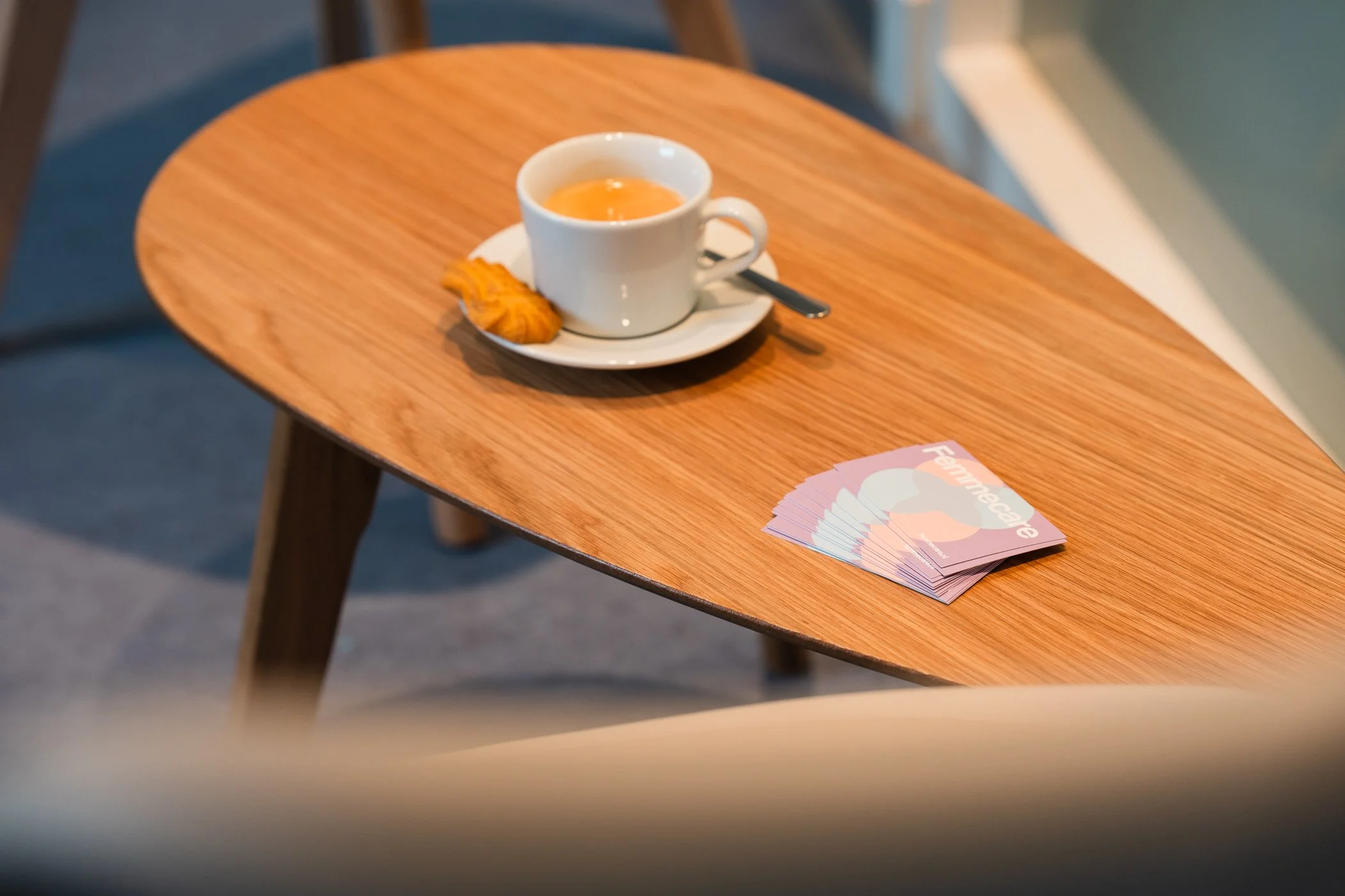 Een houten tafel met een kopje thee met een ei en een koekje, en enkele Fammecare brochures ernaast.