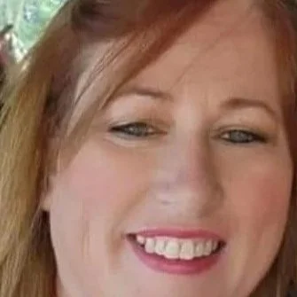 A woman with red hair and makeup posing for a photo in front of wooden paneling.