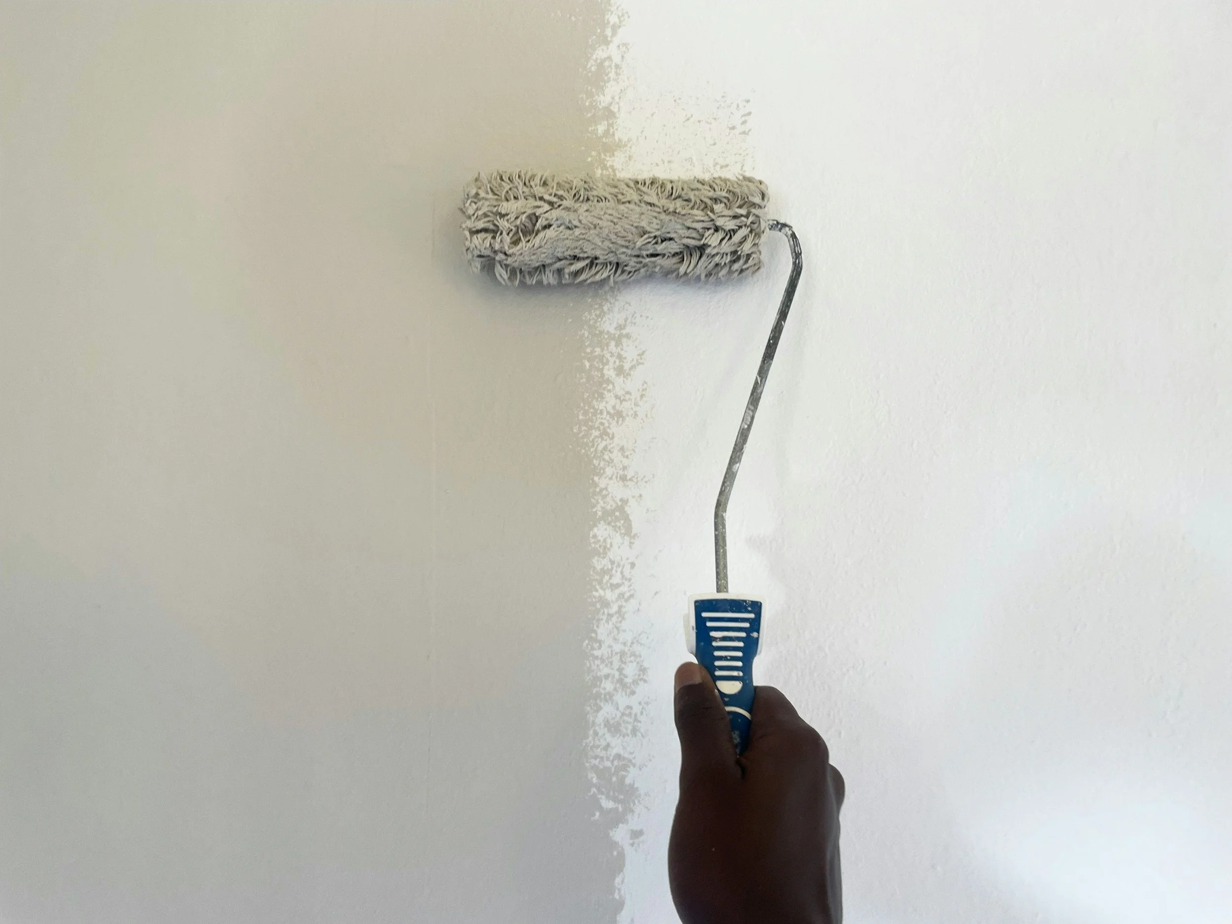 A person holding a paint roller attached to a pole, painting a white wall with white paint.