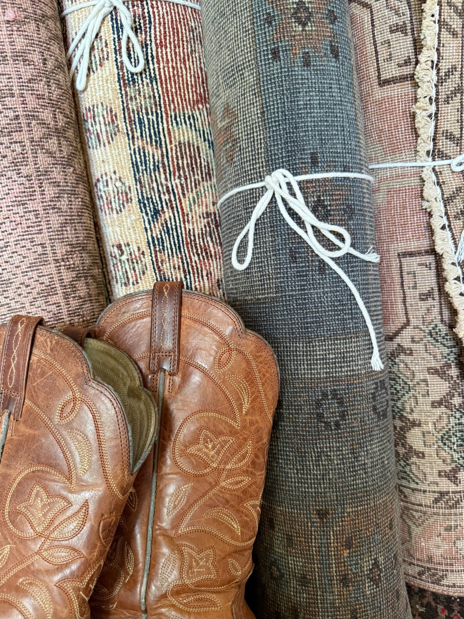 Rolled vintage rugs tied with string beside worn cowboy boots - a signature Rug Ladies look blending Texas charm with timeless handmade textiles.