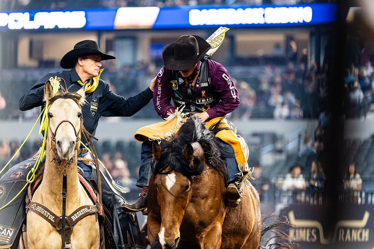 A pick up man helps a cowboy off a bucking horse after his ride.
