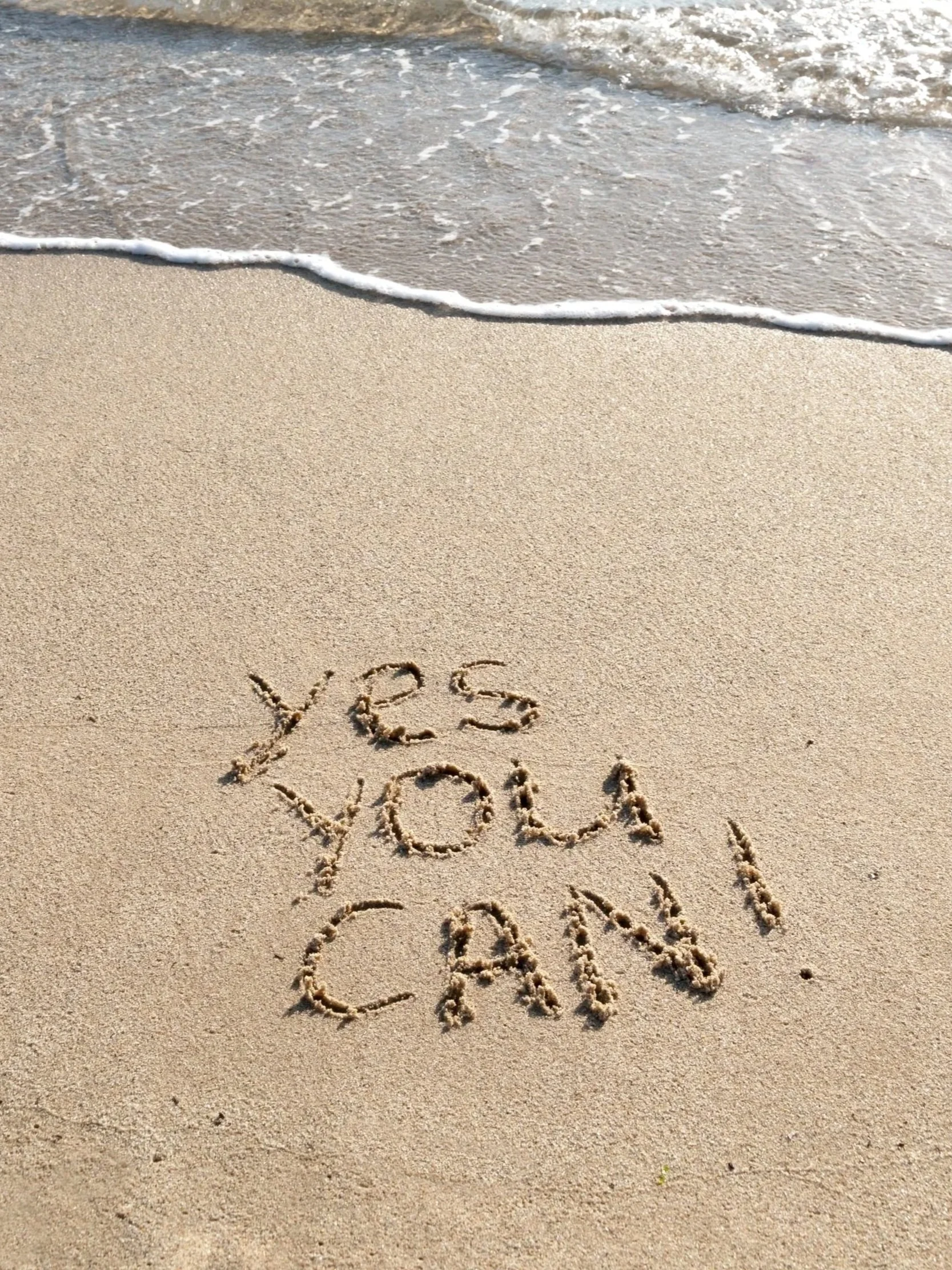 The word 'YEAH' and 'LOVE' written in the sand on a beach, with ocean waves approaching from the top of the image.