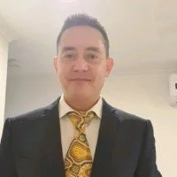 A man wearing a suit with a patterned yellow tie, smiling, standing indoors.