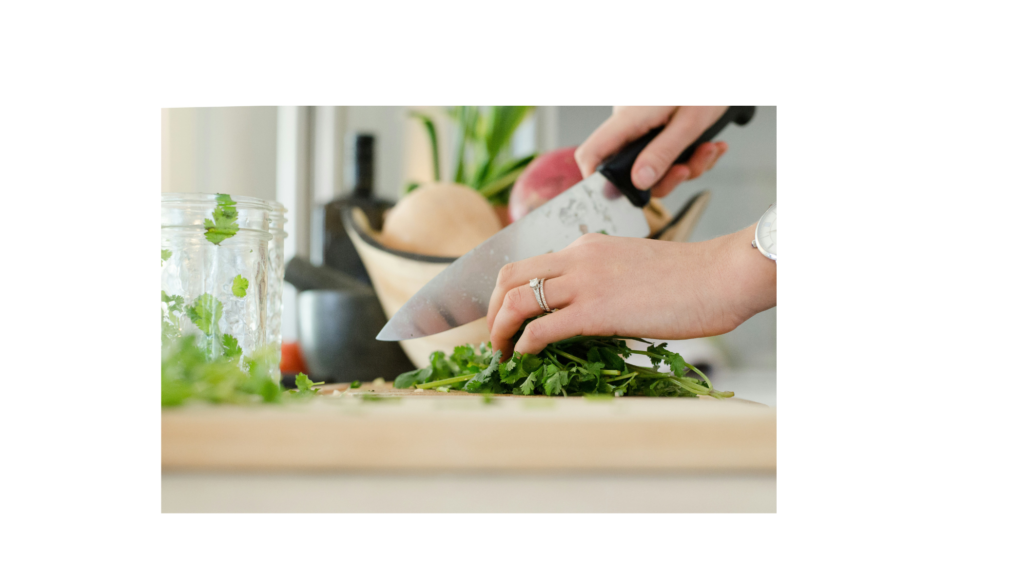 Person chopping fresh cilantro on a wooden cutting board in a bright kitchen.