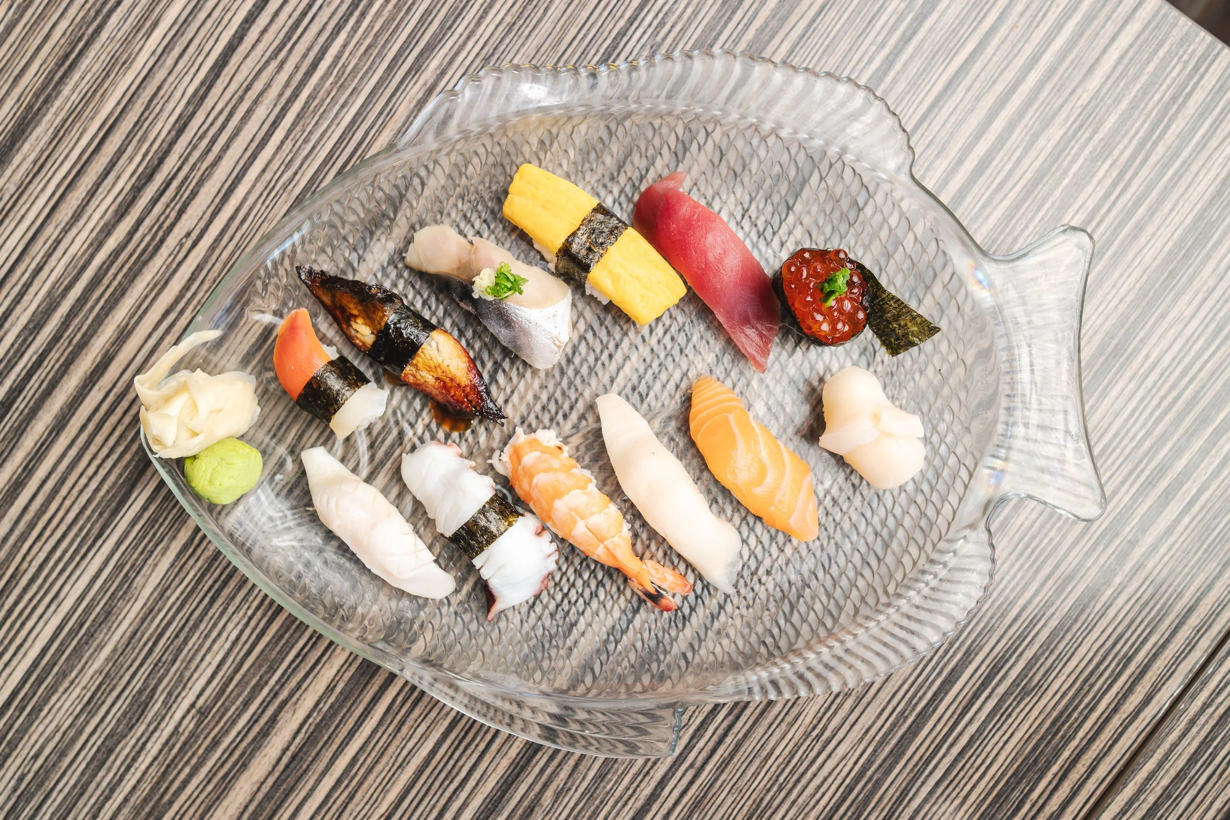 Assorted sushi pieces on a glass platter on a wooden surface.