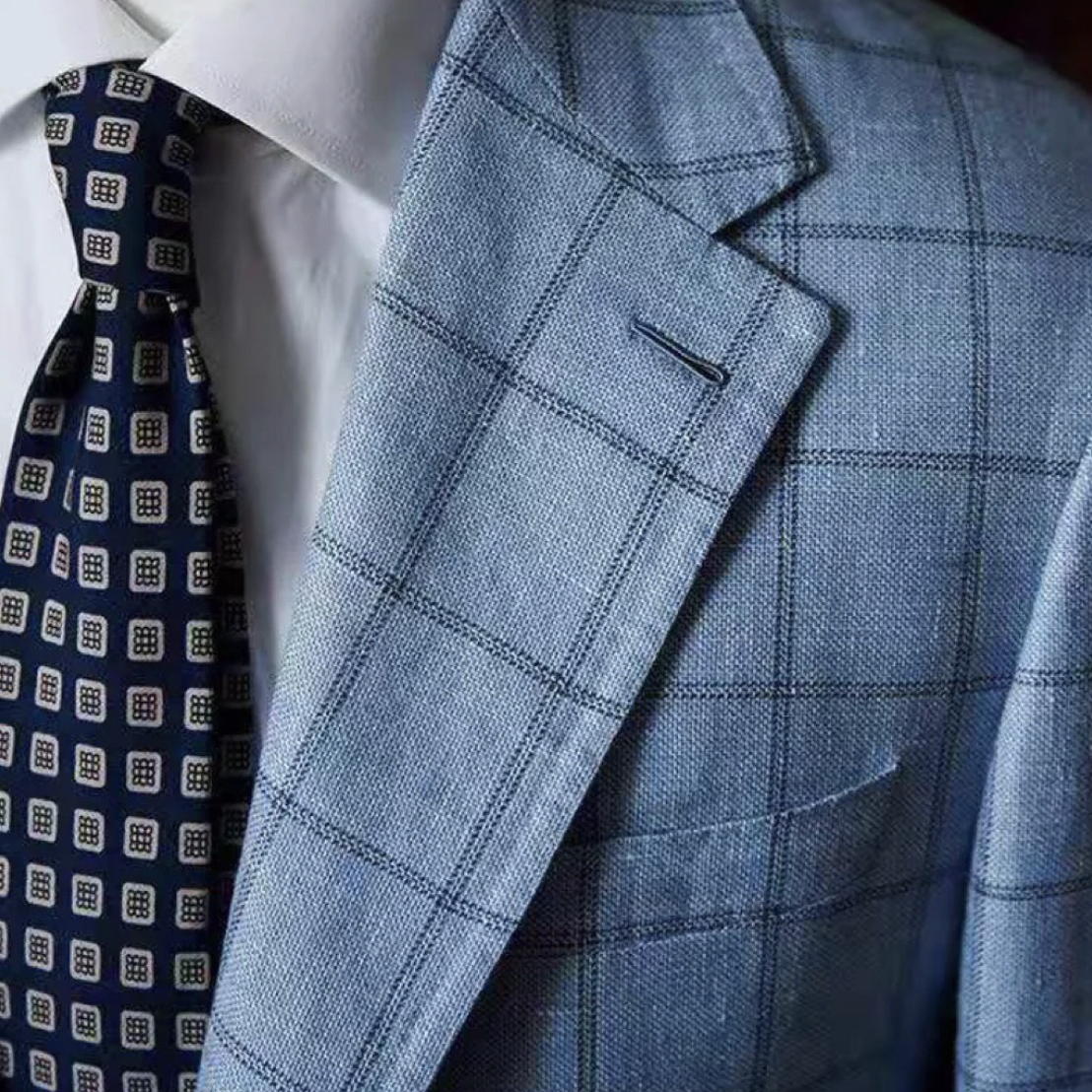 Close-up of a man wearing a white dress shirt, blue patterned tie, and light blue checked blazer.
