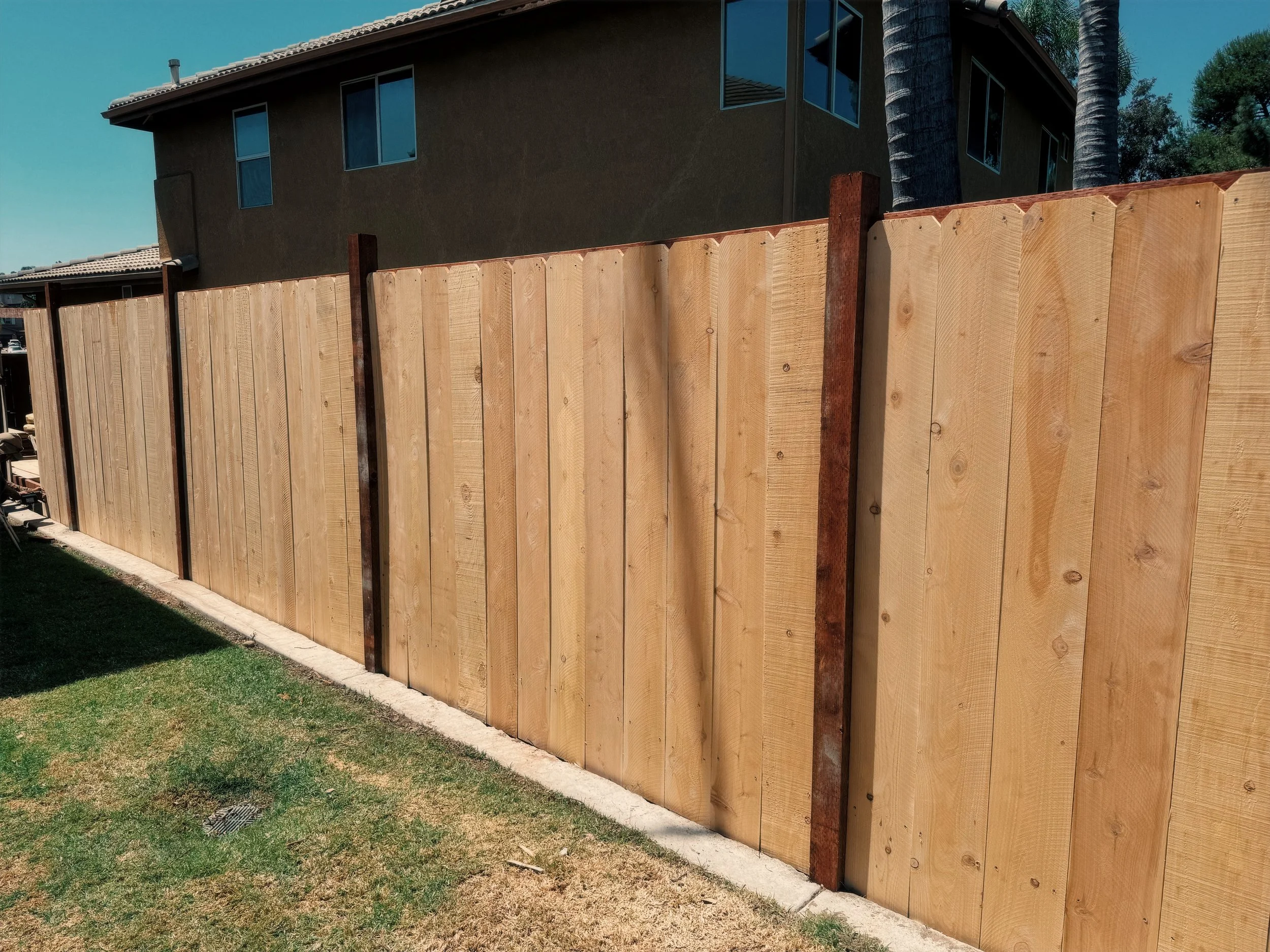 Wooden privacy fence in a backyard with grass and a house in the background.