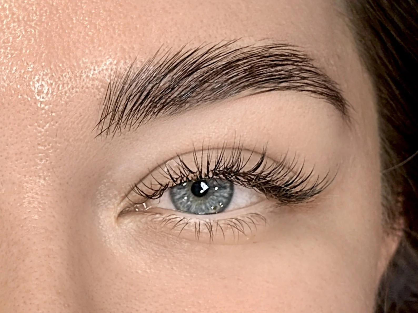 Close-up of a person's eye with blue iris, long eyelashes, and well-groomed eyebrow.