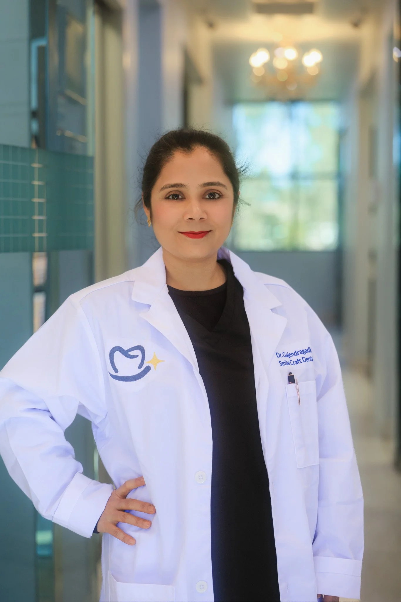 A woman dressed in a white coat standing confidently inside a modern dental clinic, smiling at the camera.