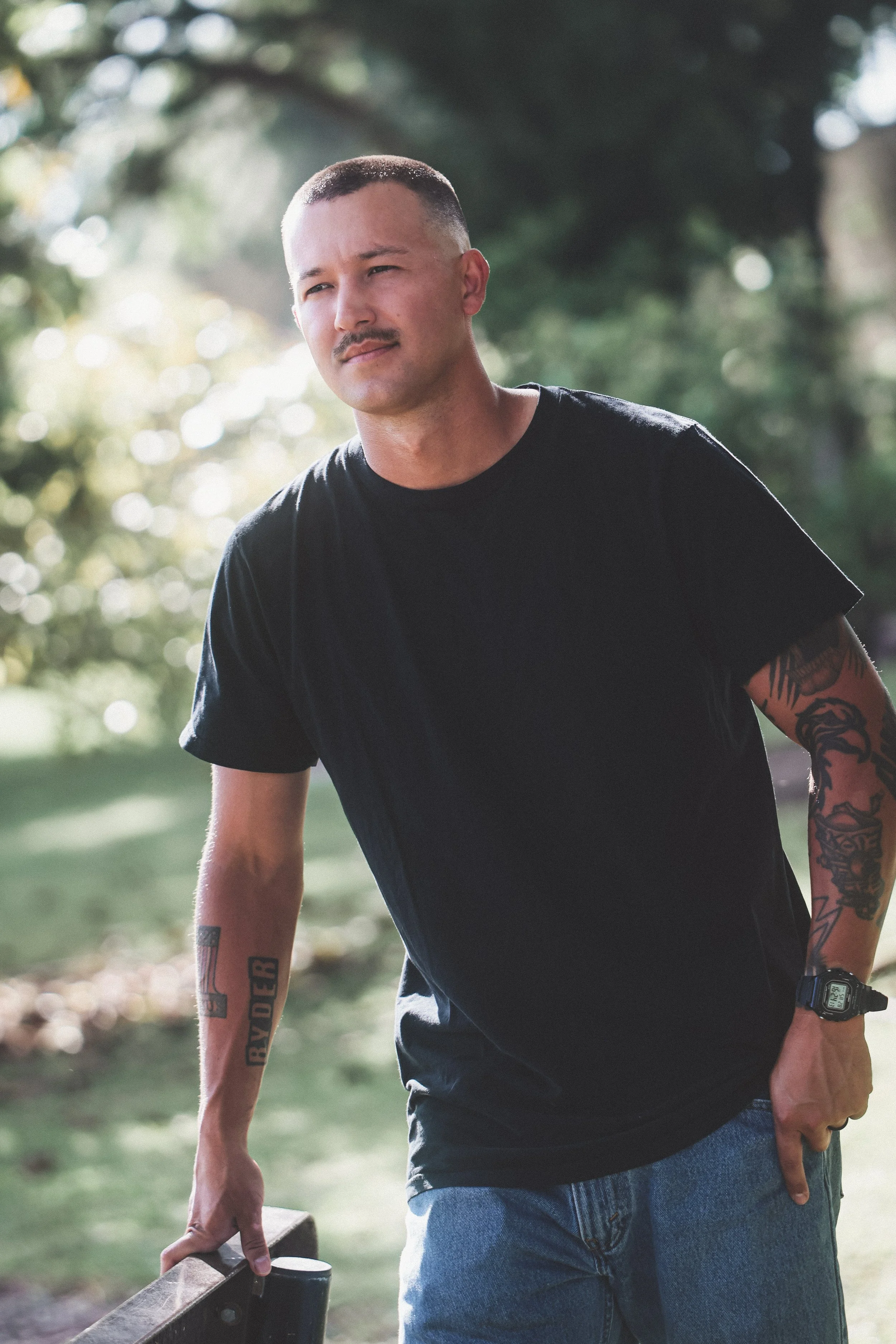 A young woman with long blonde hair wearing a black lace top, standing outdoors at sunset with the sun glowing behind her.