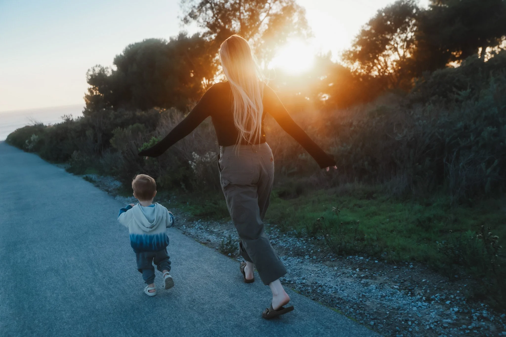 A woman and a young boy walking along a path during sunset, with the woman holding out her arms and the boy looking forward.
