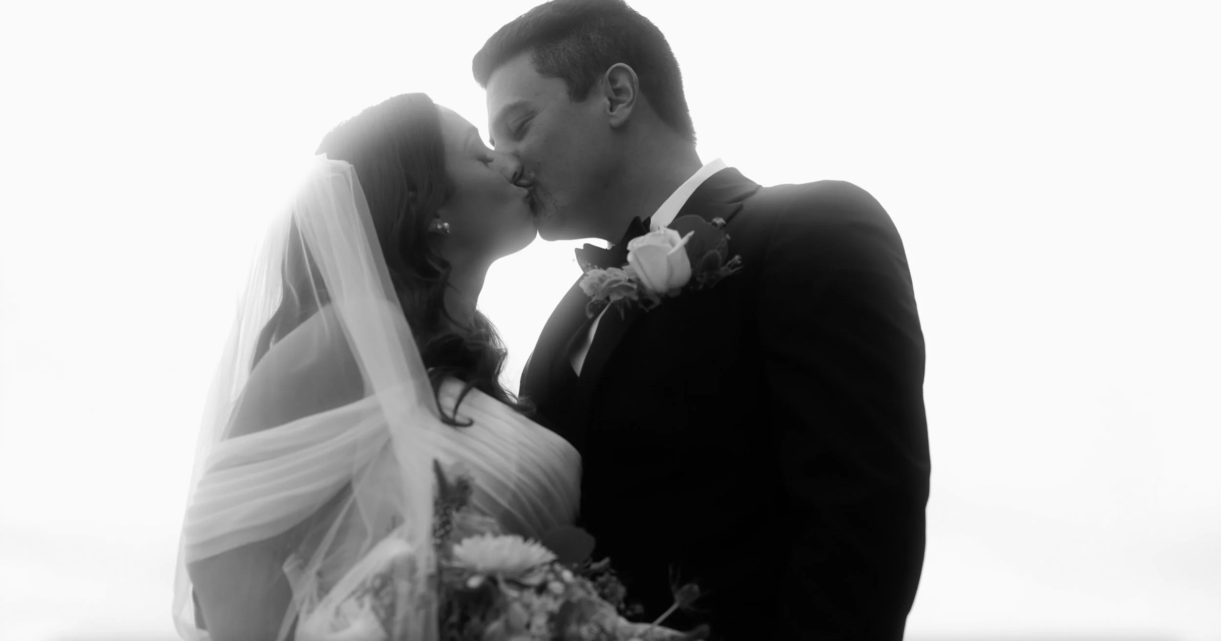 A man in a gray suit sits on a cream chair on stage with a blue background and a large screen showing a red and white thermometer graphic in the background. He has short brown hair and is wearing black combat boots with red socks.