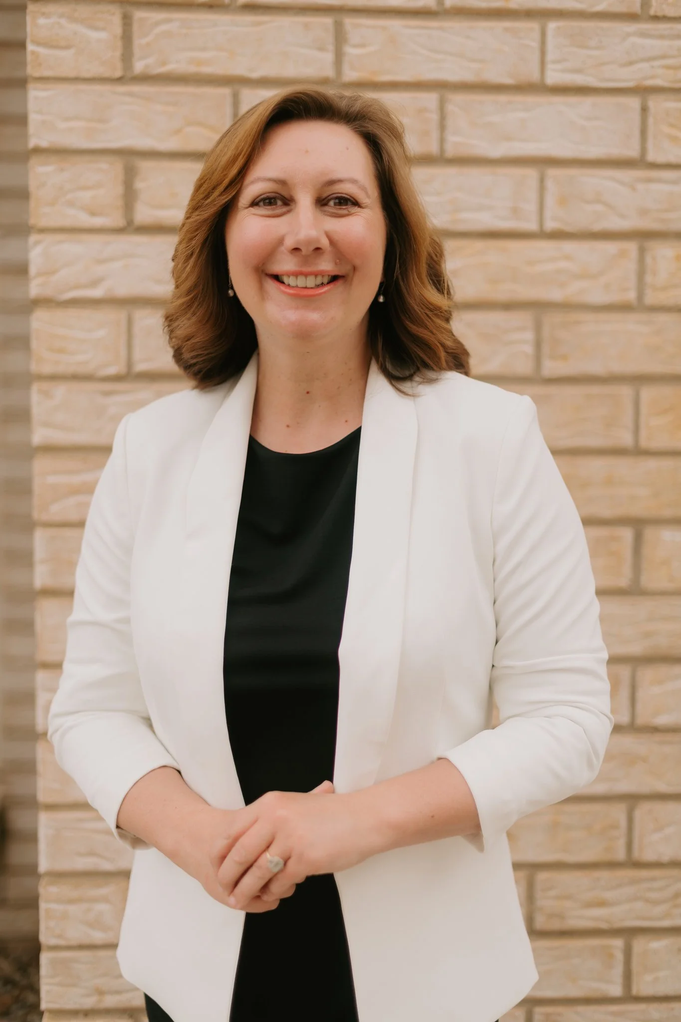 Maree Bryant, Governance, Risk and Assurance consultant with shoulder-length brown hair, smiling, standing in front of a beige brick wall, wearing a white blazer over a black top.