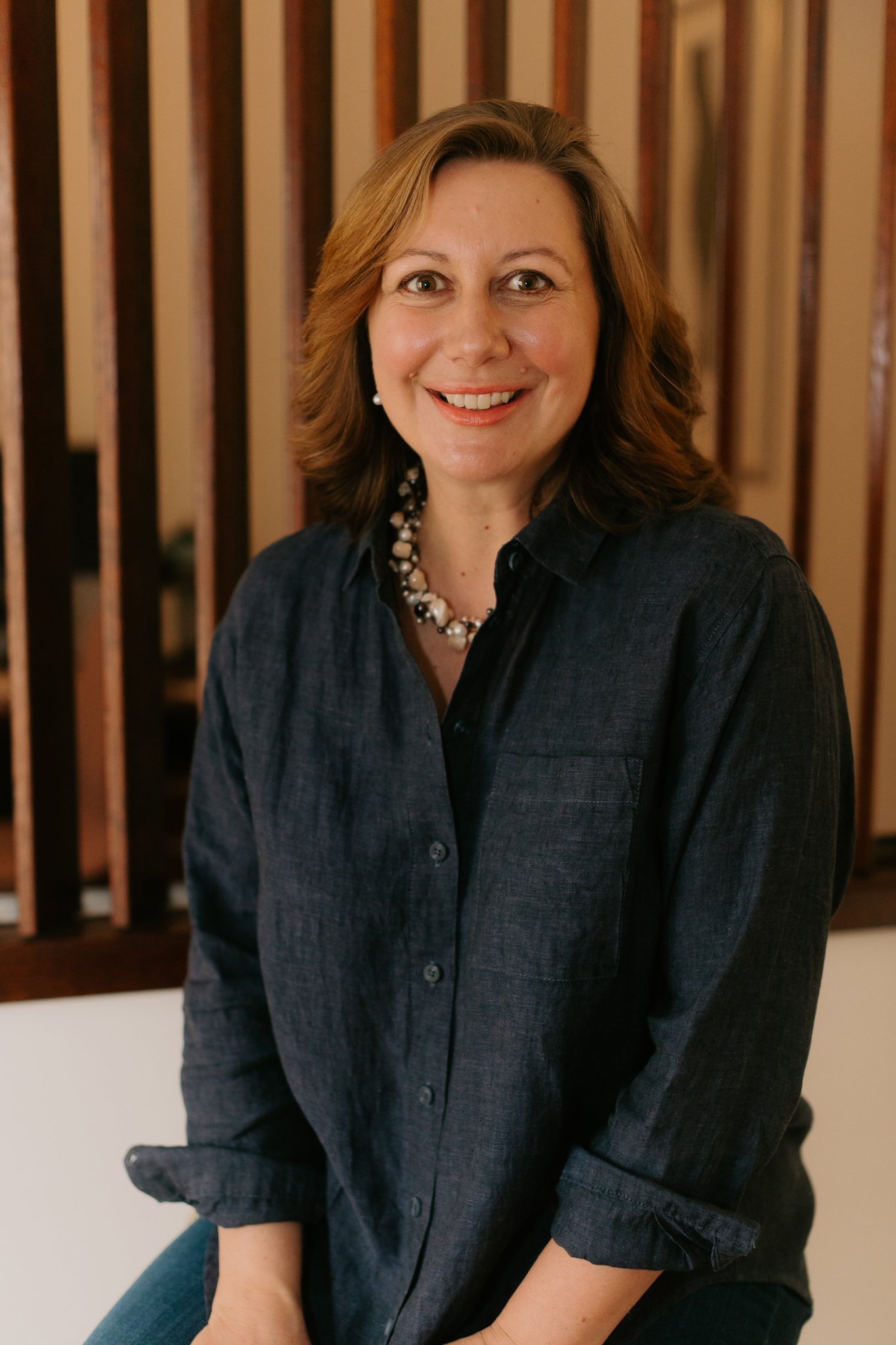 Maree Bryant, Governance, Risk and Assurance consultant with shoulder-length hair wearing a dark button-up shirt and a pearl necklace, sitting indoors with a wooden partition in the background.