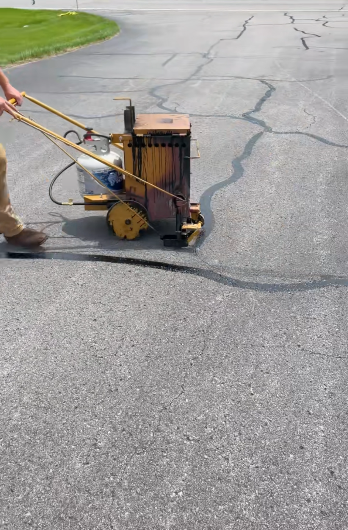 A person operating a Crack sealing machine on a paved asphalt road.