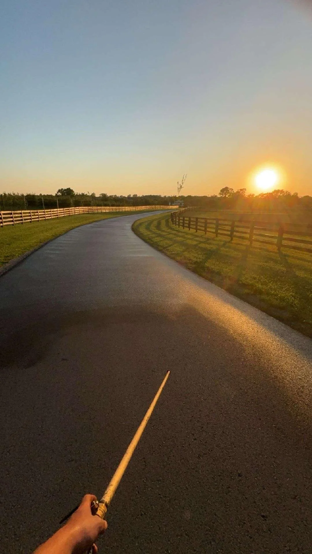 A photo of a Sealcoat paved farm road during sunset, with green grass and wooden fences on either side.