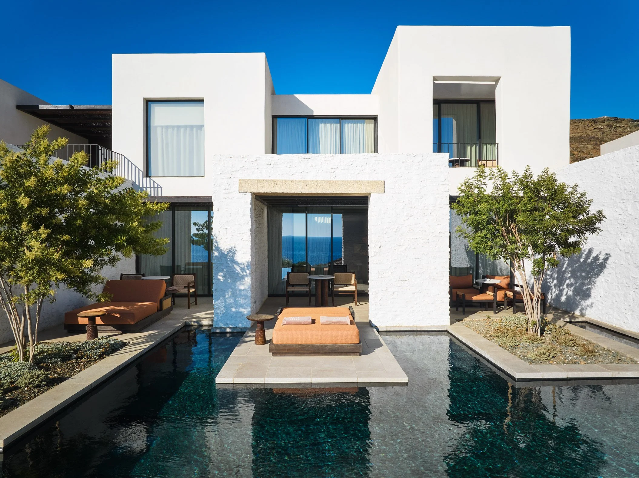 Modern white house with outdoor terrace, pool, and ocean view in the background.