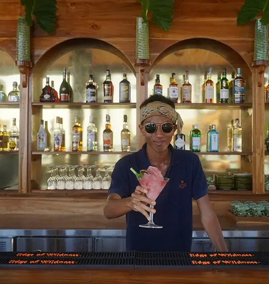 A bartender holding a pink cocktail garnished with a lime wedge and a celery stalk.