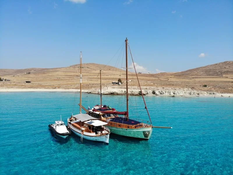 Three boats anchored in clear blue water along a dry, hilly landscape under a blue sky.