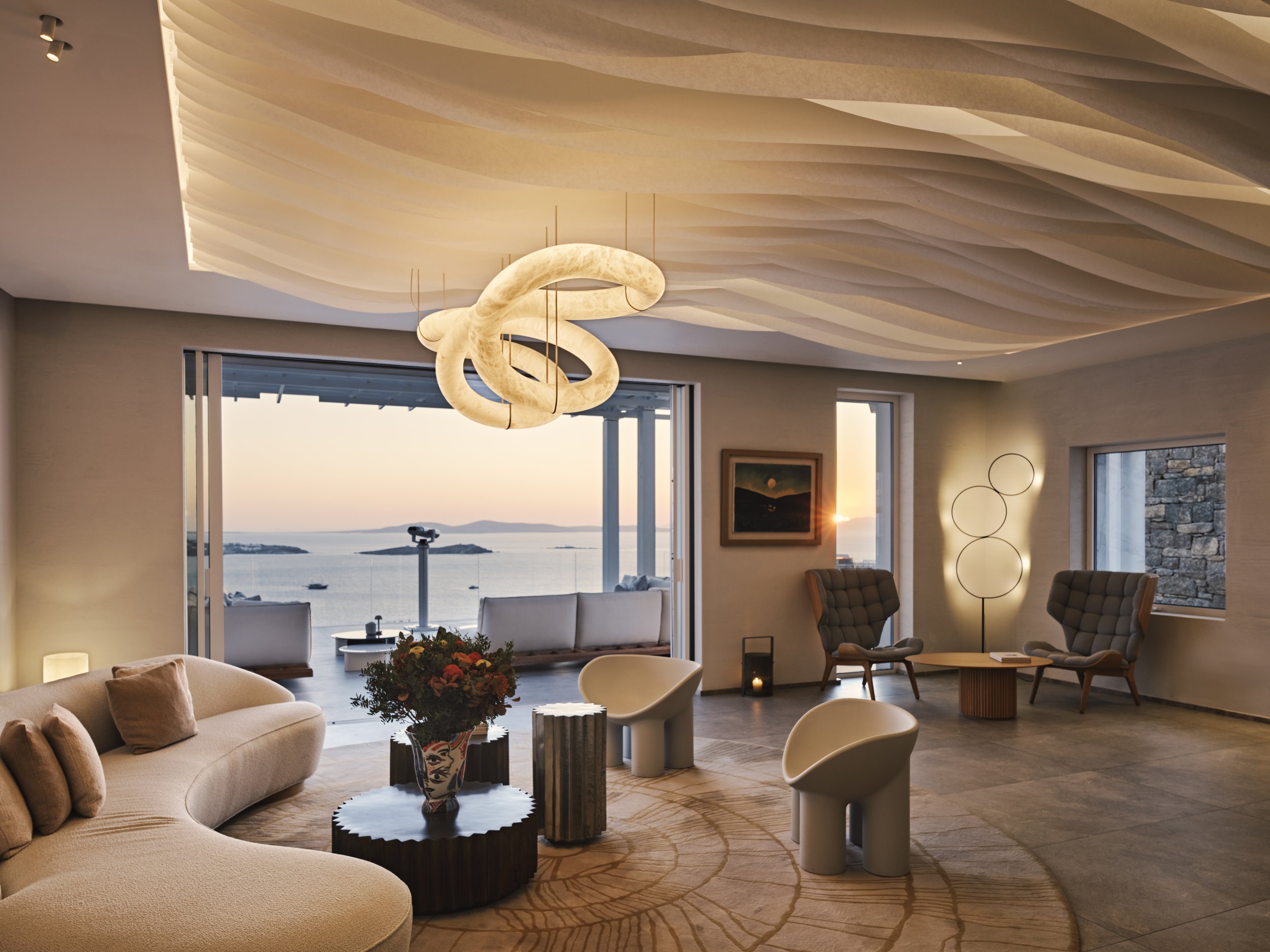Living room with ocean view, modern furniture, and decorative lighting at sunset.