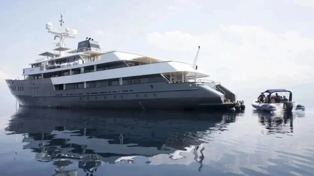 A large yacht floating on calm water alongside a smaller inflatable boat with people.
