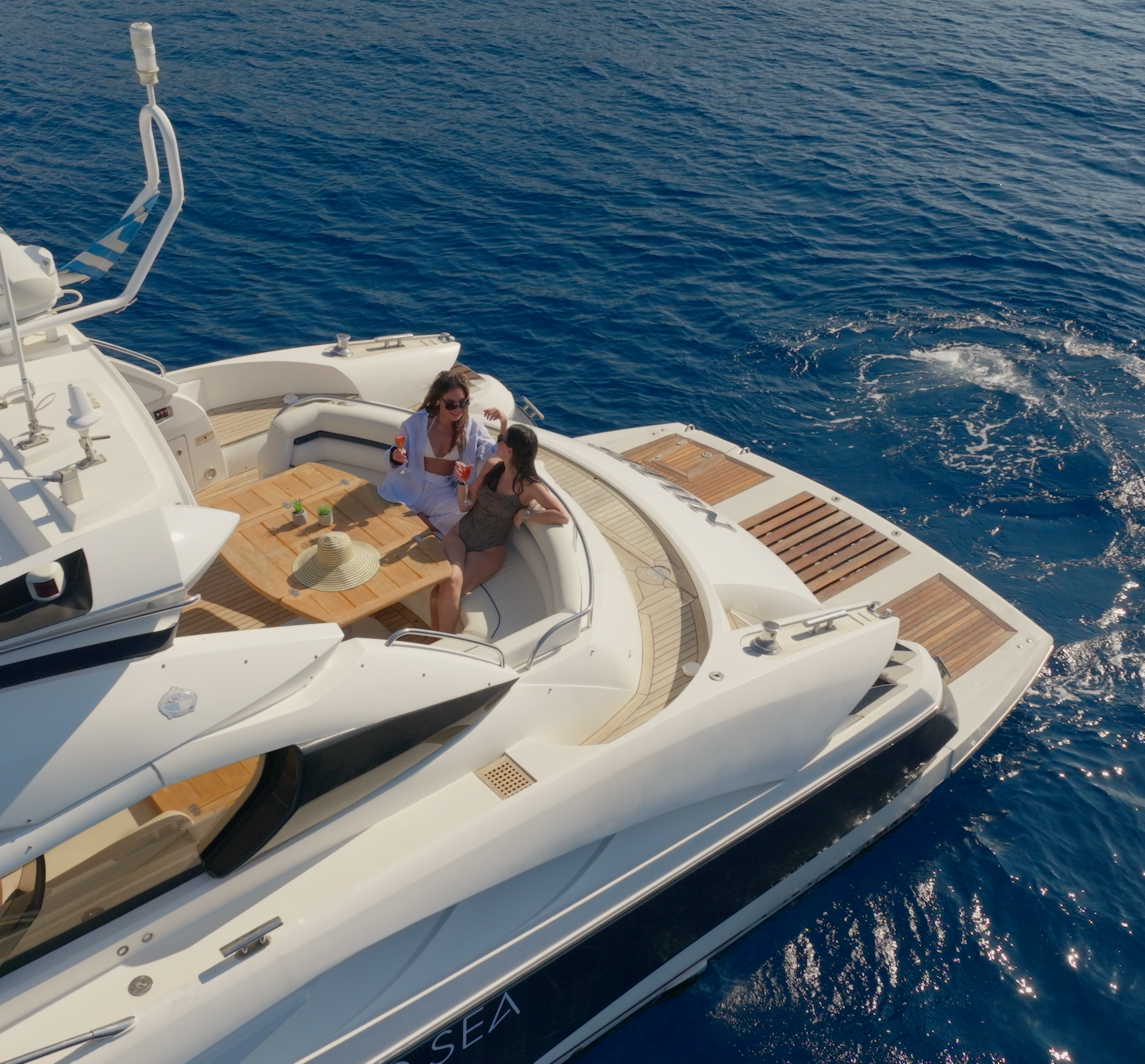 Two women on a white yacht enjoying drinks and chatting, with the ocean in the background.