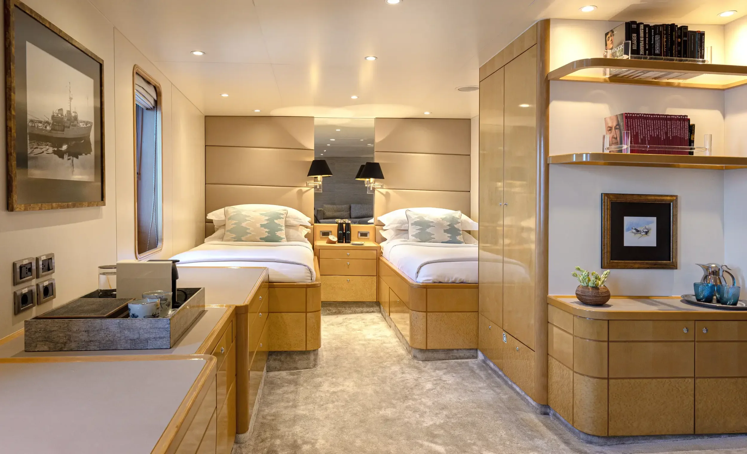 A modern hotel room with two beds, a small sitting area, and built-in wooden furniture and shelves.