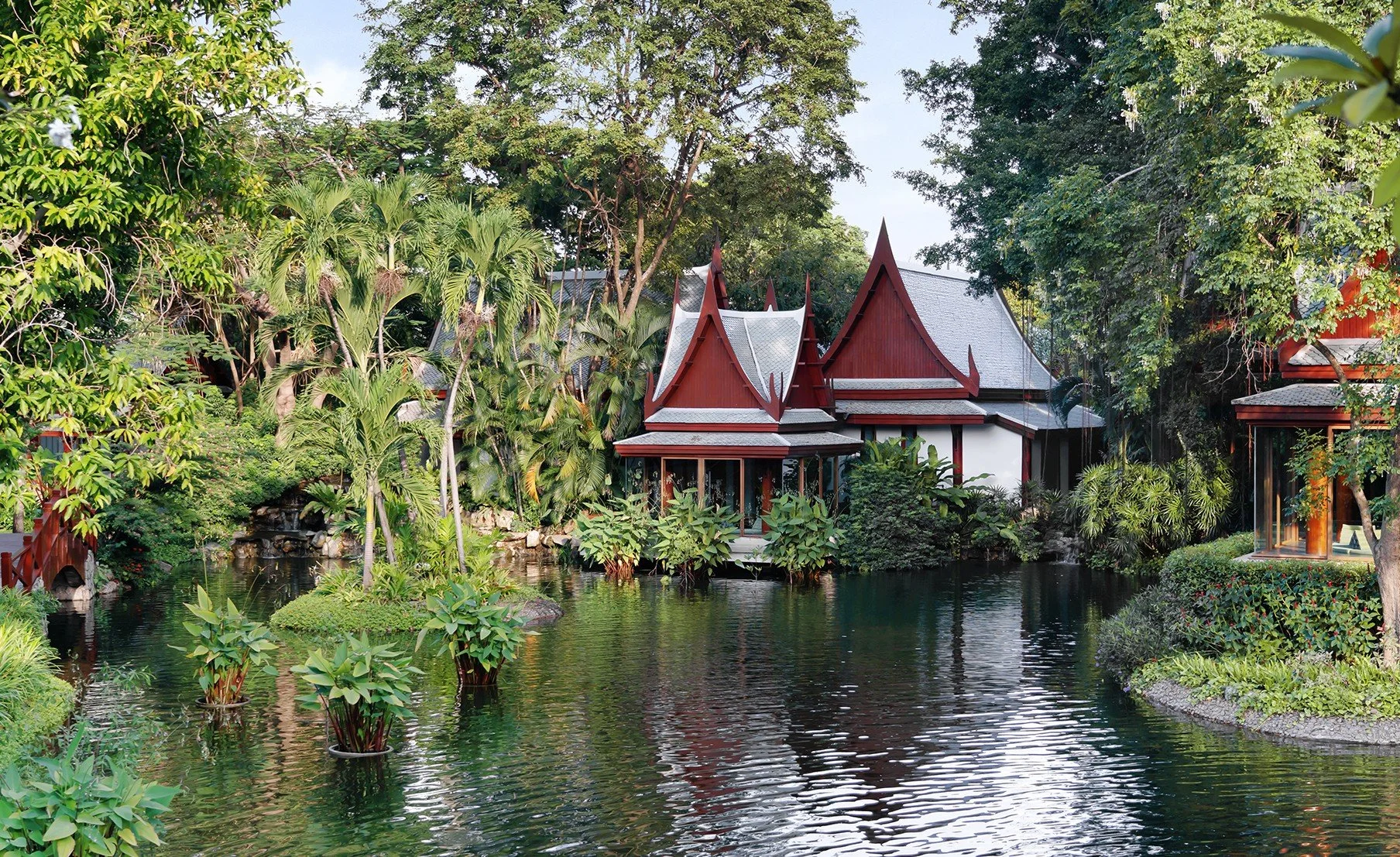 Traditional Thai-style buildings surrounded by lush greenery and a pond.