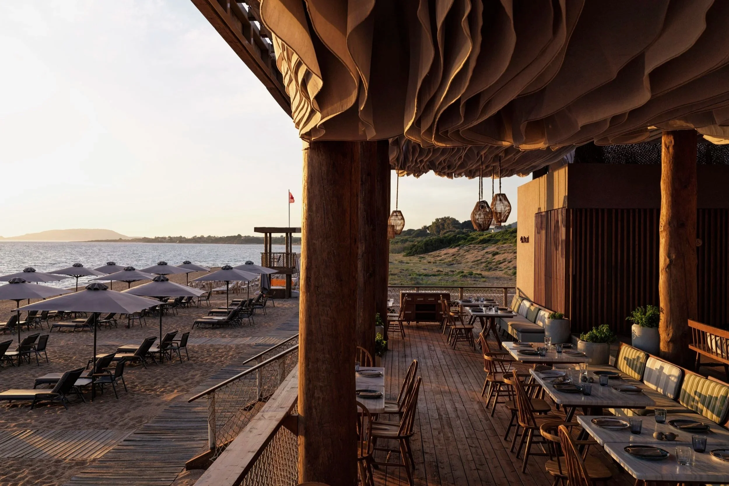 Empty beachfront restaurant with outdoor tables and umbrellas, overlooking the ocean at sunset.