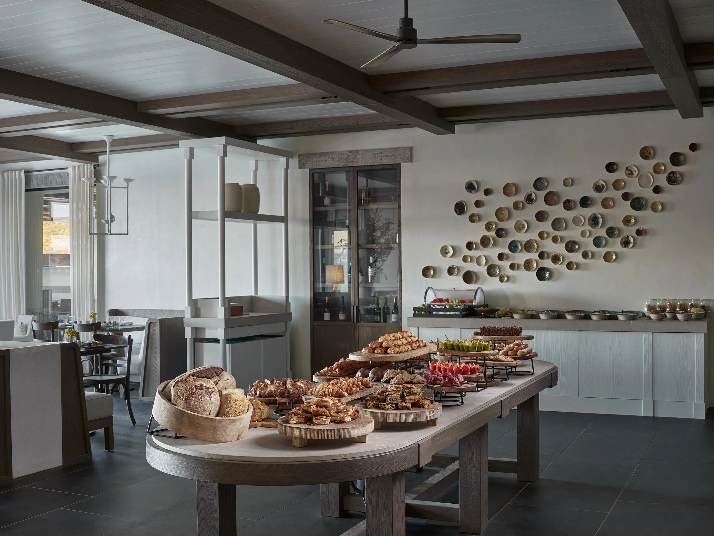 A buffet table with bread, pastries, and fruit in a modern dining area with artwork on the wall.