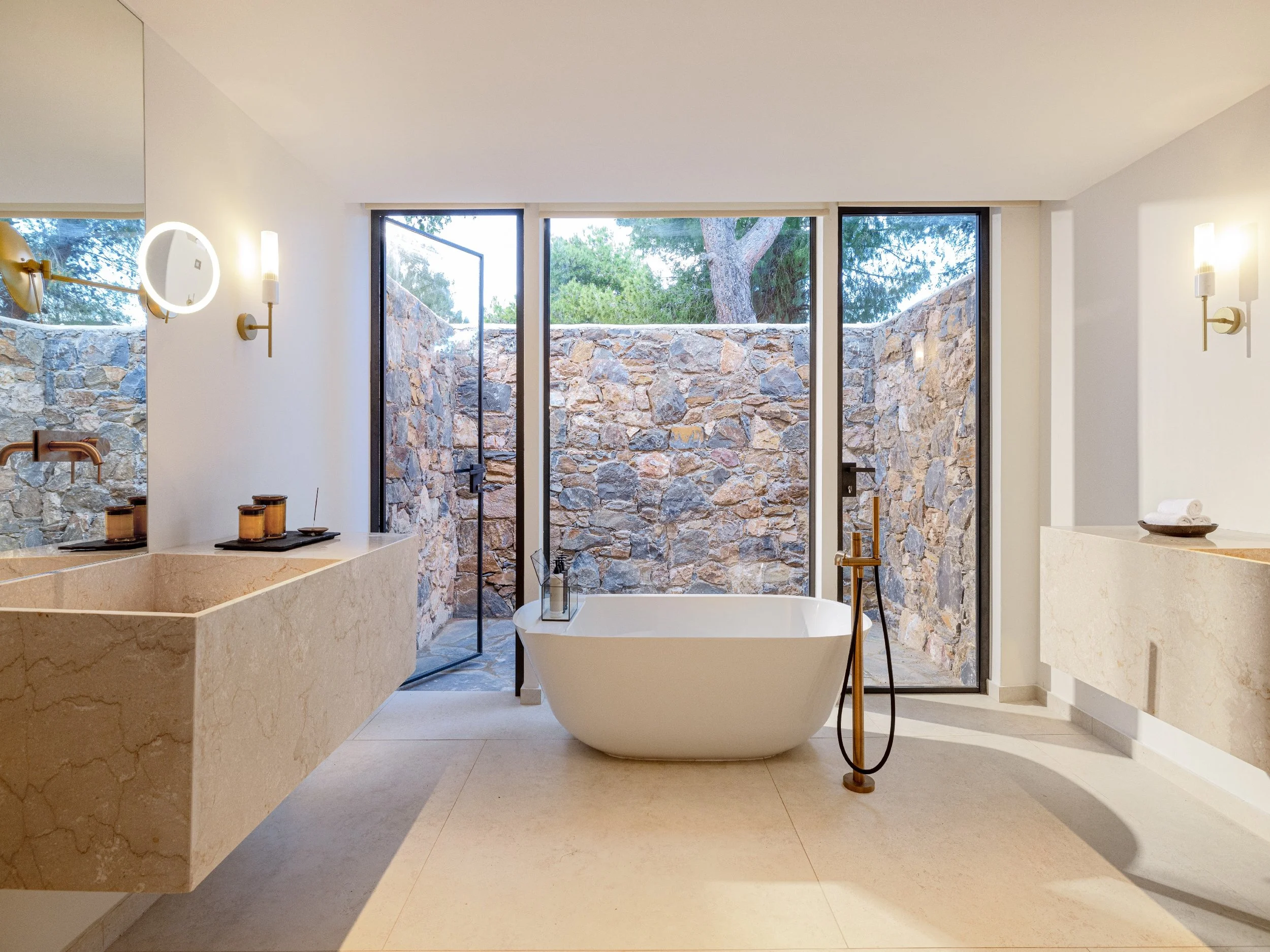 Modern bathroom with bathtub, stone wall, glass doors, and minimal decor.