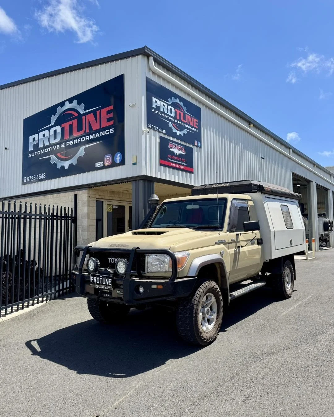 A beige Toyota Land Cruiser parked outside a building with signs for Pro Tune Automotive & Performance.
