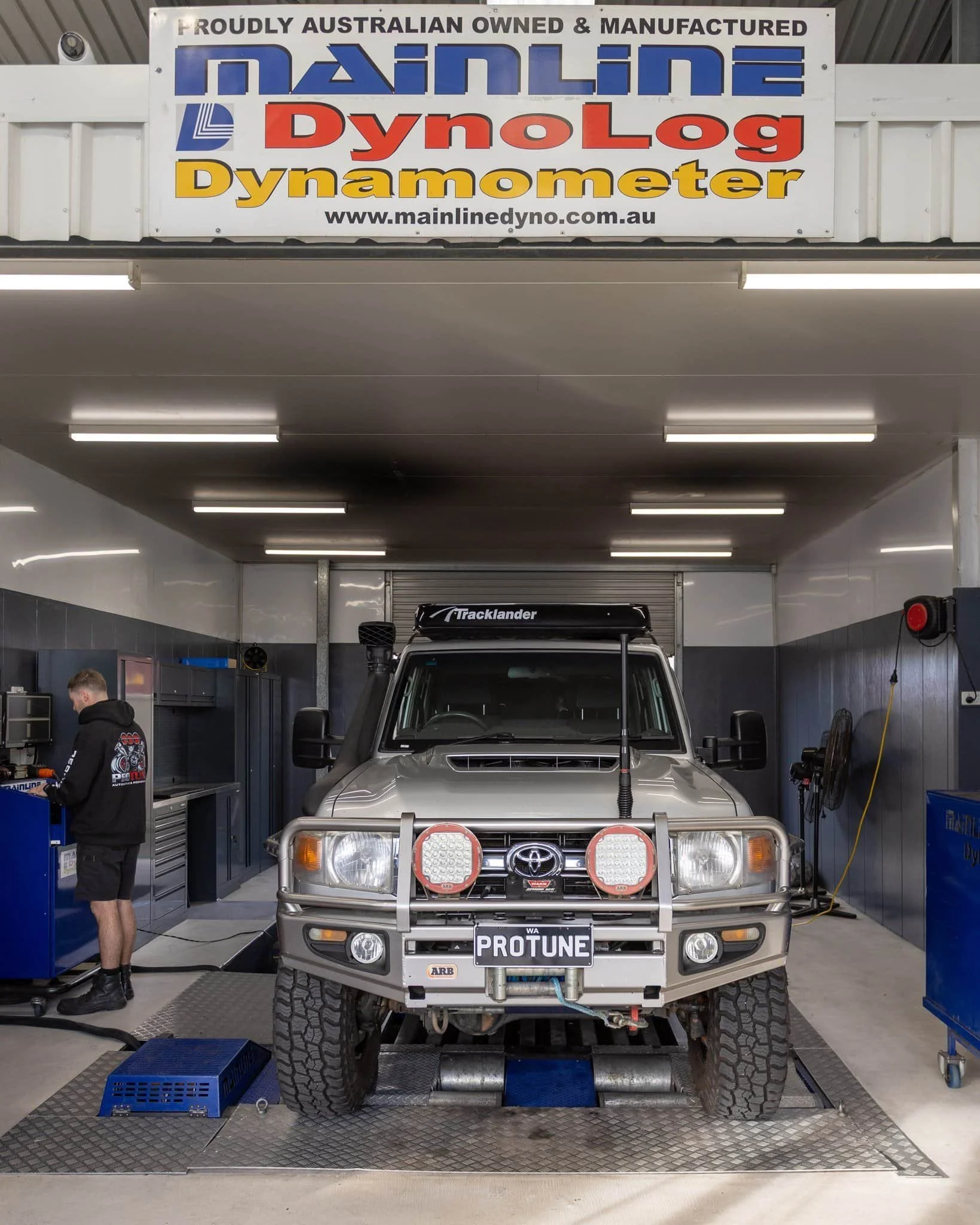 An off-road Toyota vehicle inside a workshop with a sign above indicating it is an Australian-owned Dynalog Dynamometer station. The vehicle has a bull bar with two round LED lights and a license plate that reads 'PROTUNE'.