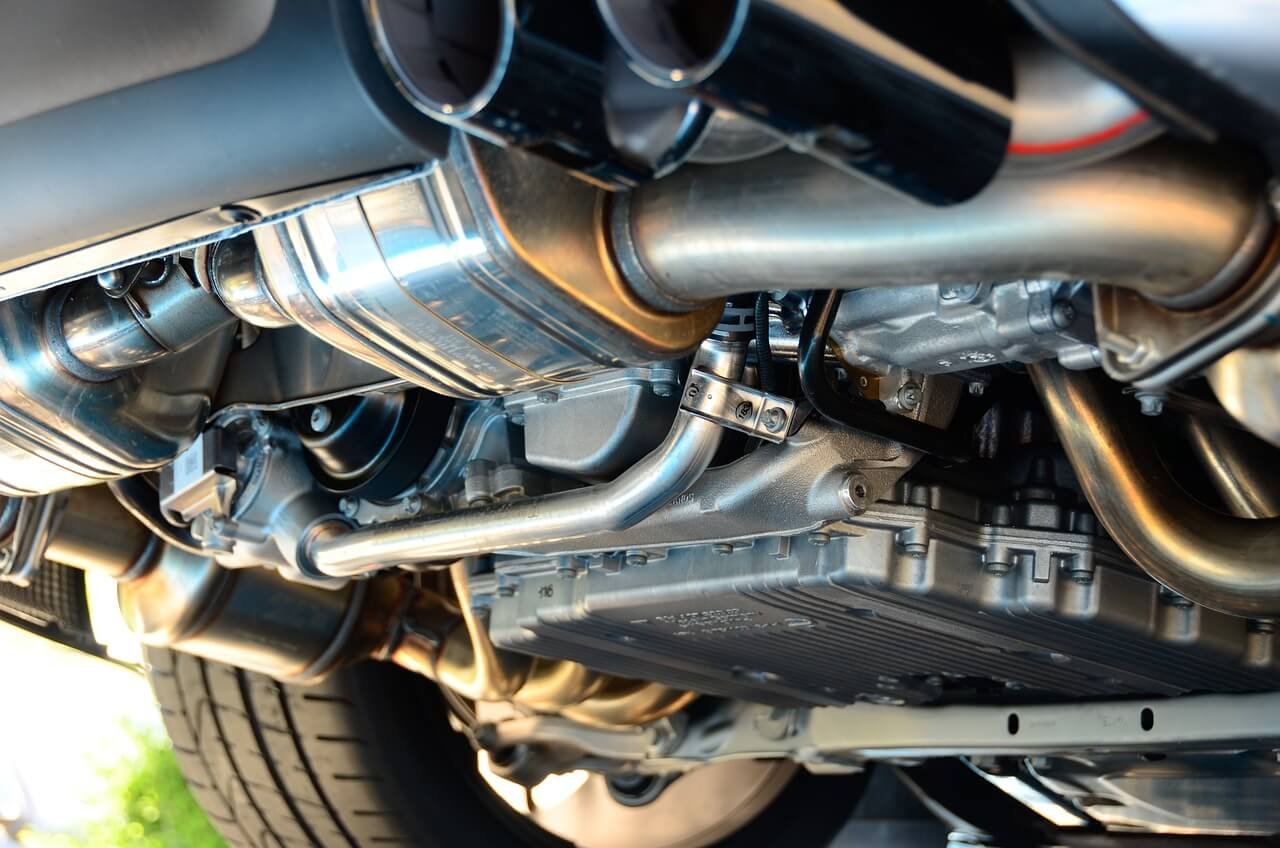 Close-up view of a car's undercarriage showing engine components, pipes, and the underside of the vehicle.