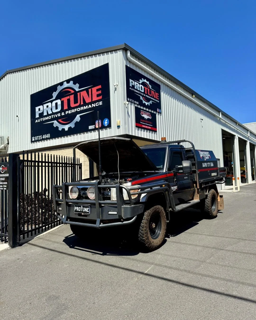 A black utility truck with an open hood parked outside an automotive performance shop called ProTune, with signage on the building. The building has a metal exterior and a large sign displaying the company logo.