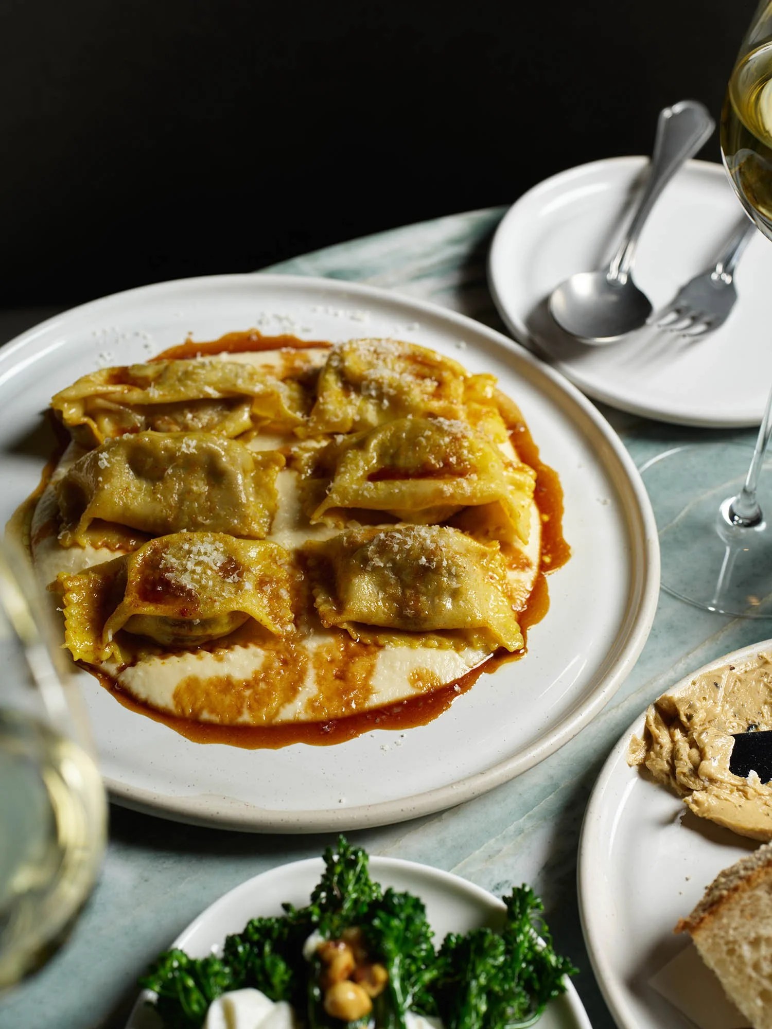 Plate of pasta with cheese and tomato sauce, and a side of bread, with wine and cutlery on a table.