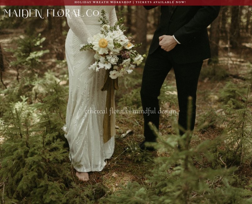 A bride and groom standing barefoot in a forest, holding a bouquet of flowers, with a banner at the top advertising holiday wreath workshop and tickets. The bride wears a white dress, and the groom wears a black suit.