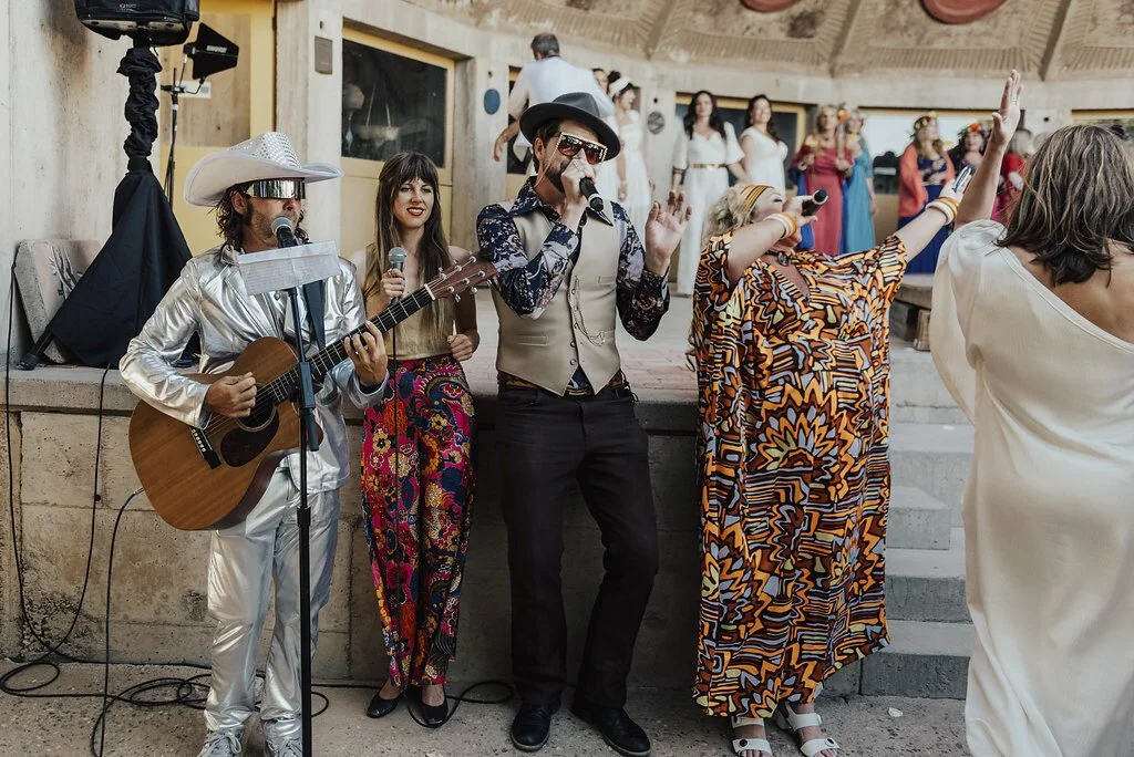 People performing and dancing at a lively indoor celebration with a musician playing guitar, singer, and dancers in colorful attire.