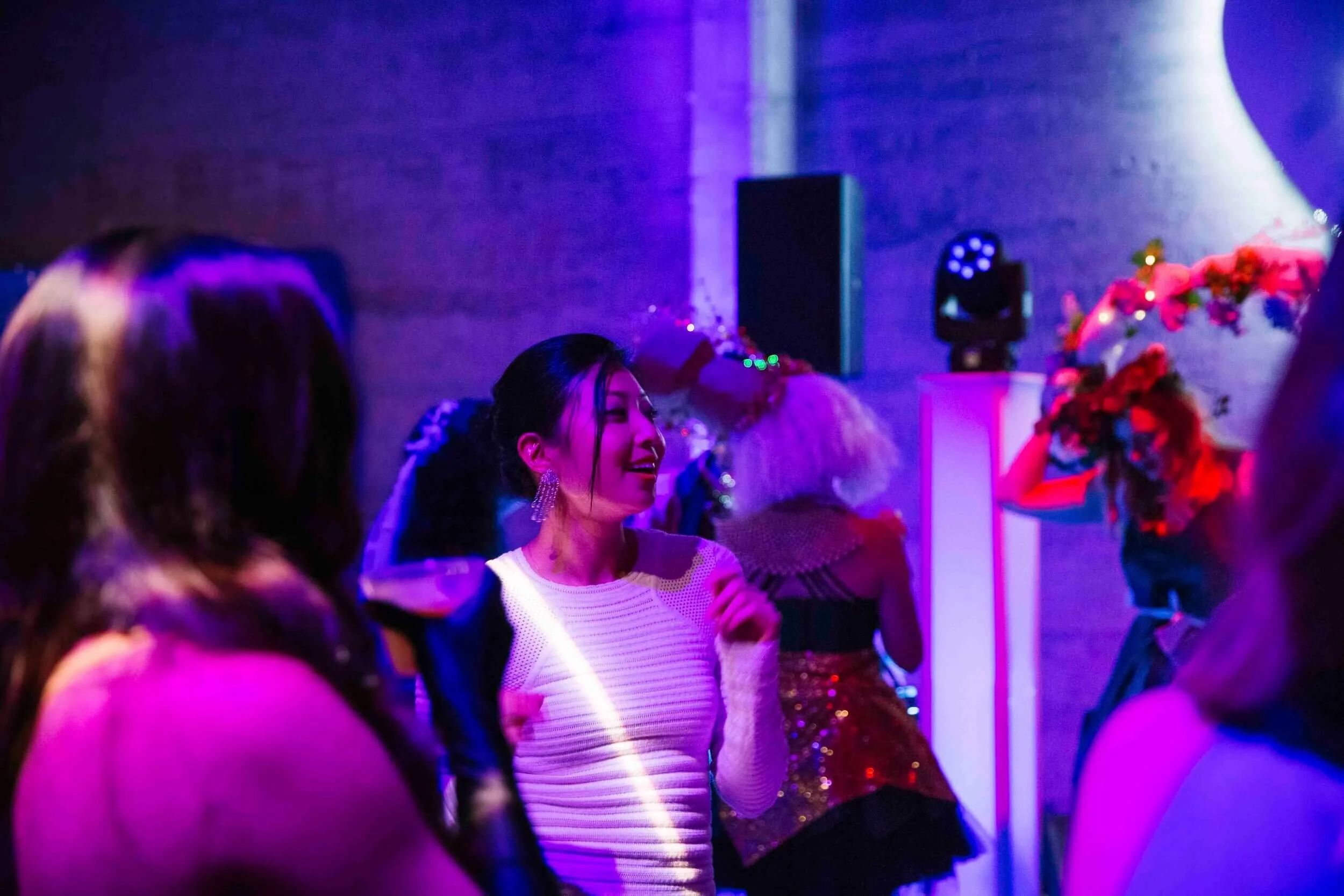 People dancing and socializing at a party with colorful lighting and floral decorations.