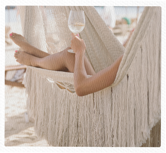Person relaxing in a hammock with legs stretched out, holding a glass of wine.