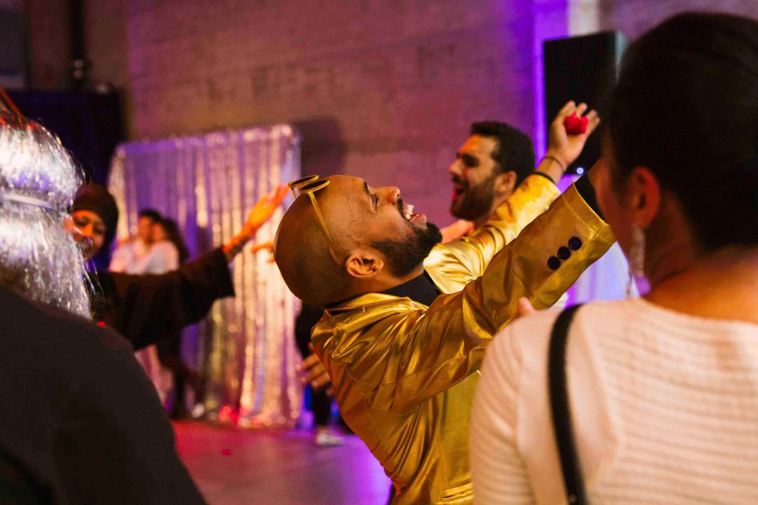People dancing and celebrating at a lively party, with colorful lighting and joyful expressions.
