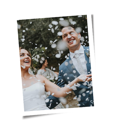 A newlywed couple celebrating with confetti at their wedding, smiling and joyful.