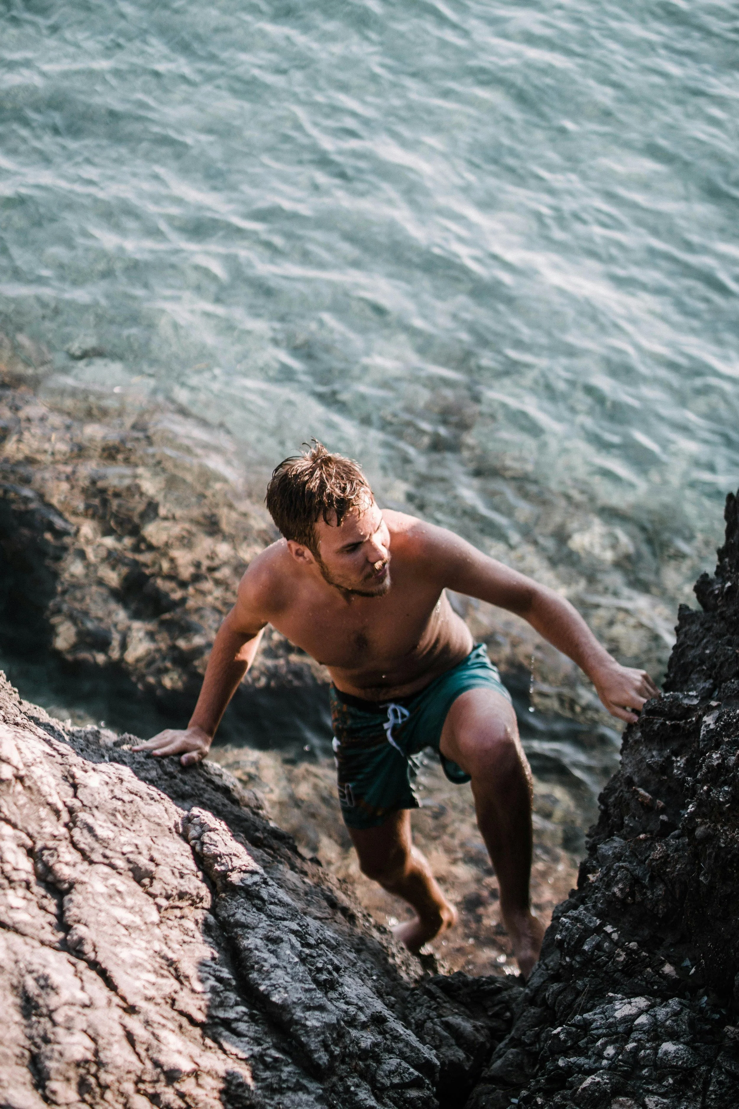A shirtless man climbing out of water on a rocky shoreline, symbolizing individual therapy and the journey of affordable relationship counselling