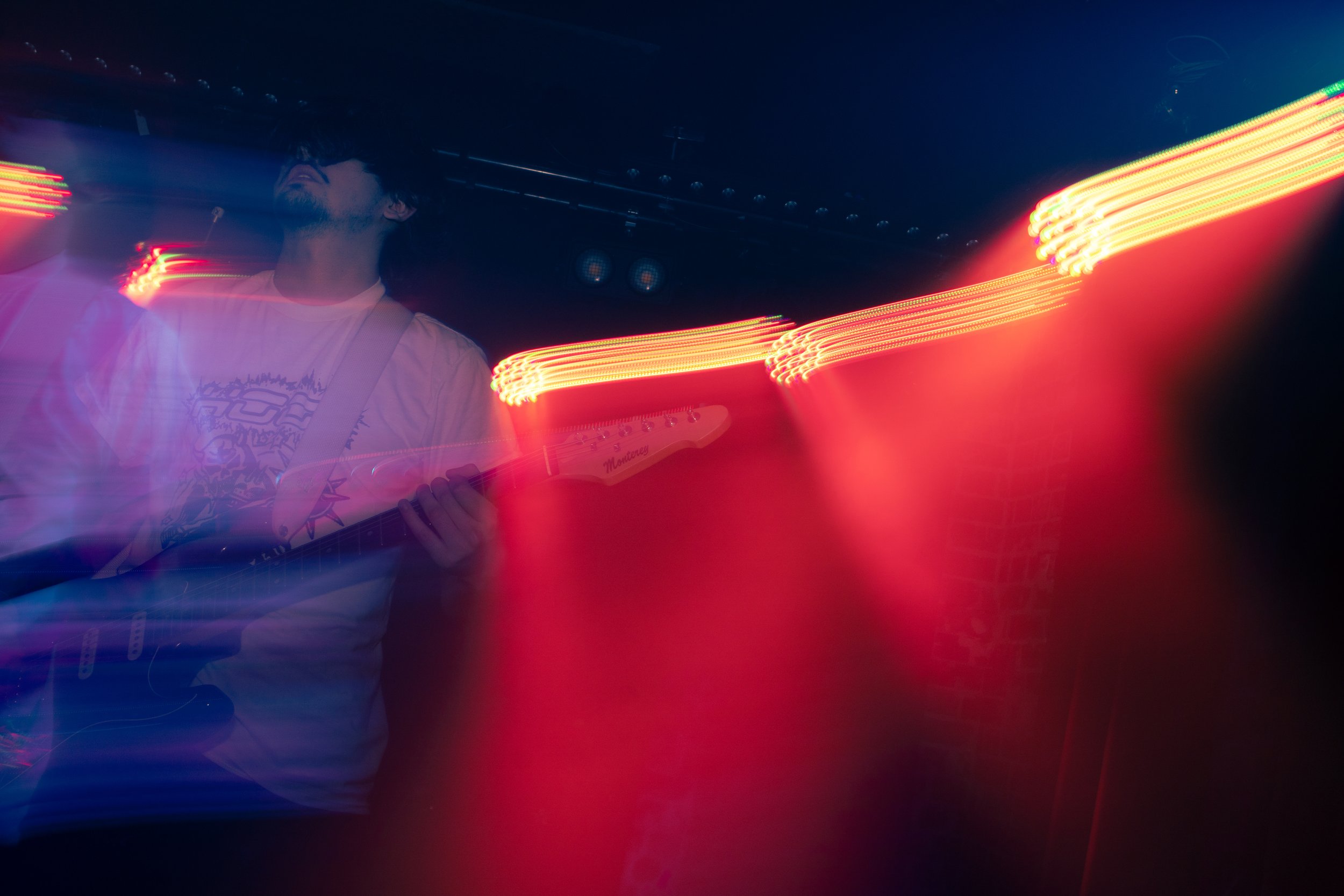 A person playing an electric guitar on stage with colorful light streaks and dark background, creating a dynamic and energetic scene.