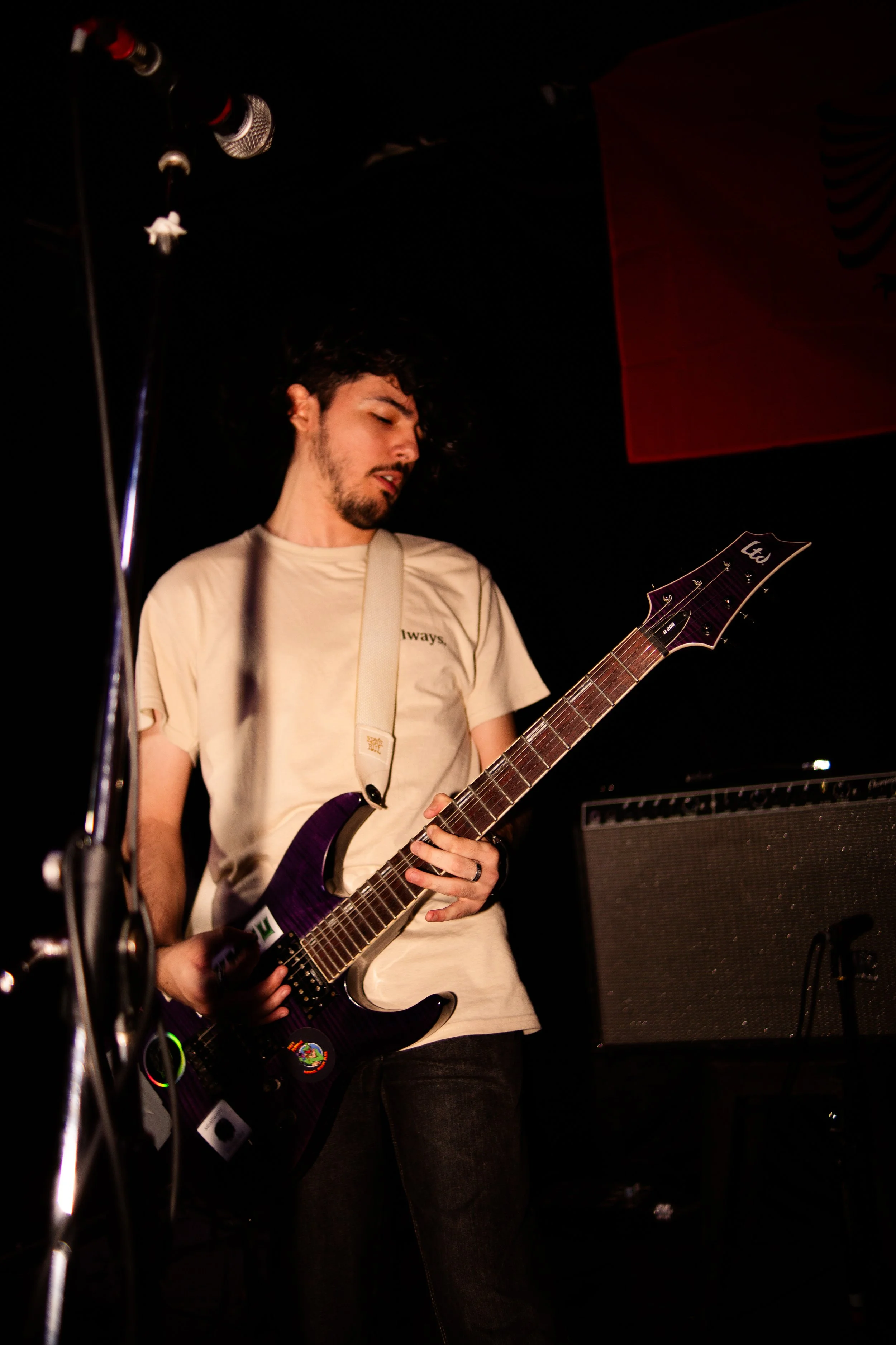 A young man playing an electric guitar on stage with a microphone and amplifier in the background.