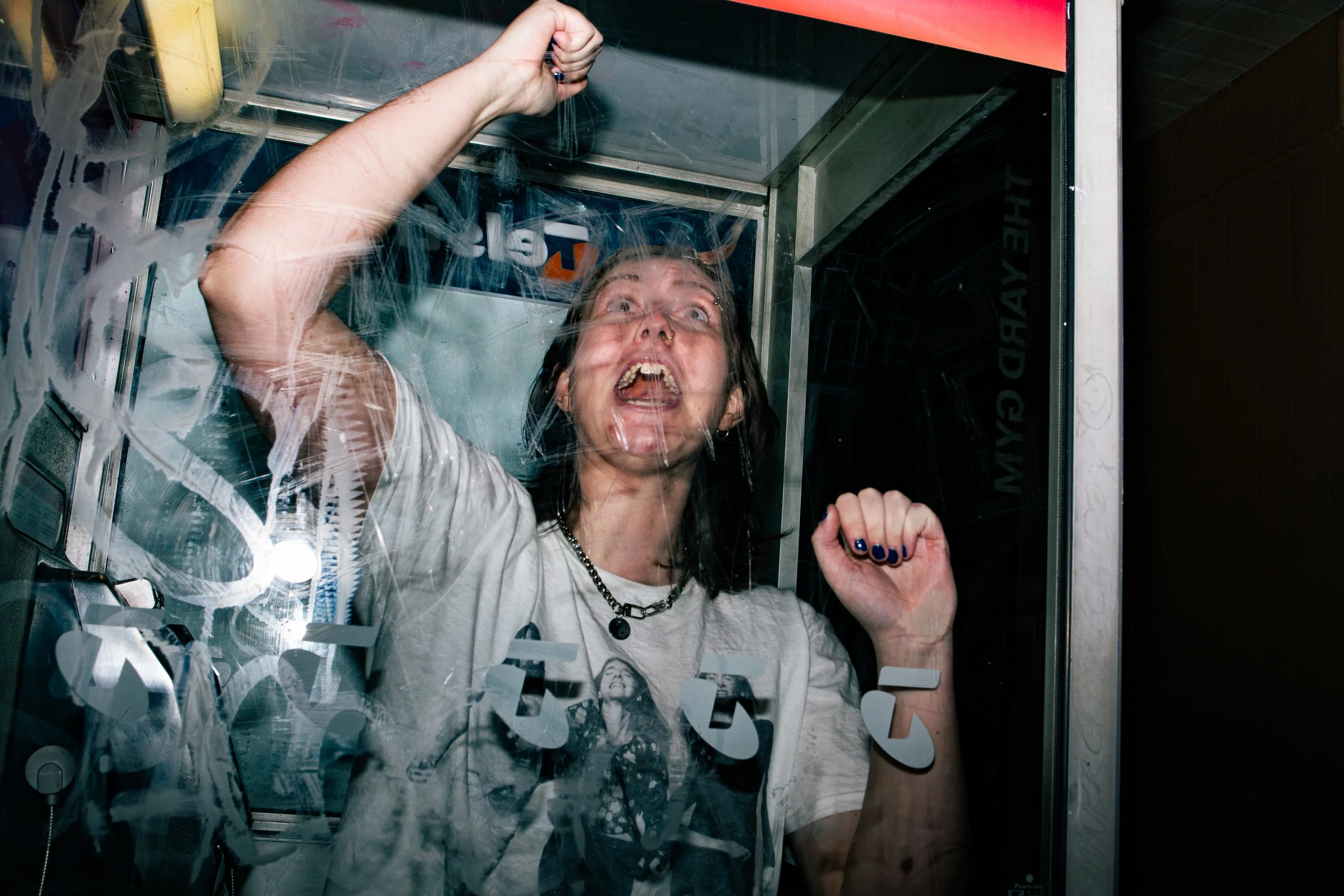 Woman inside a glass phone booth, pushing on the glass with her hand and expressing frustration or anger.