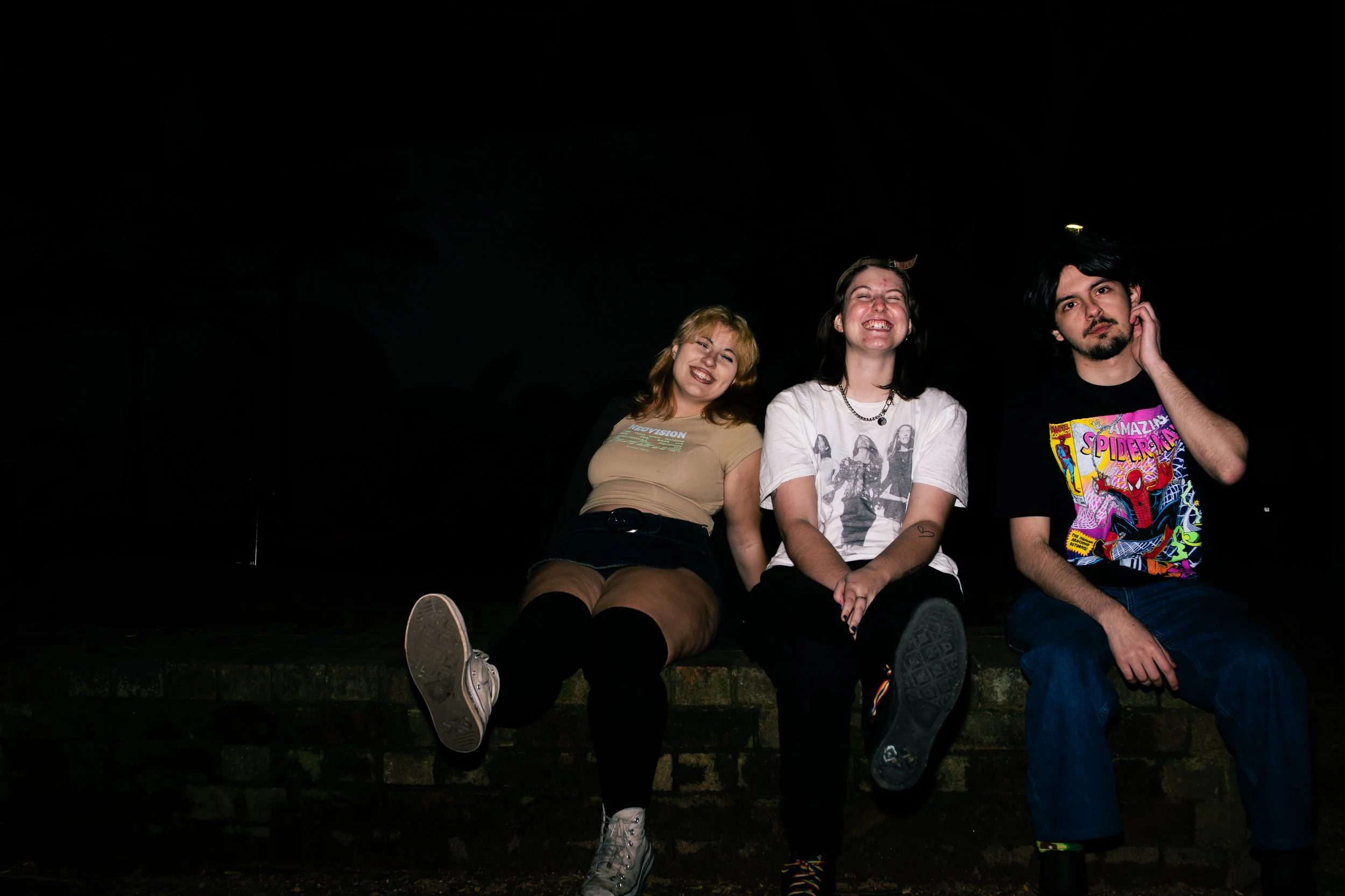 Three people sitting on a brick ledge at night, smiling and posing for the camera.