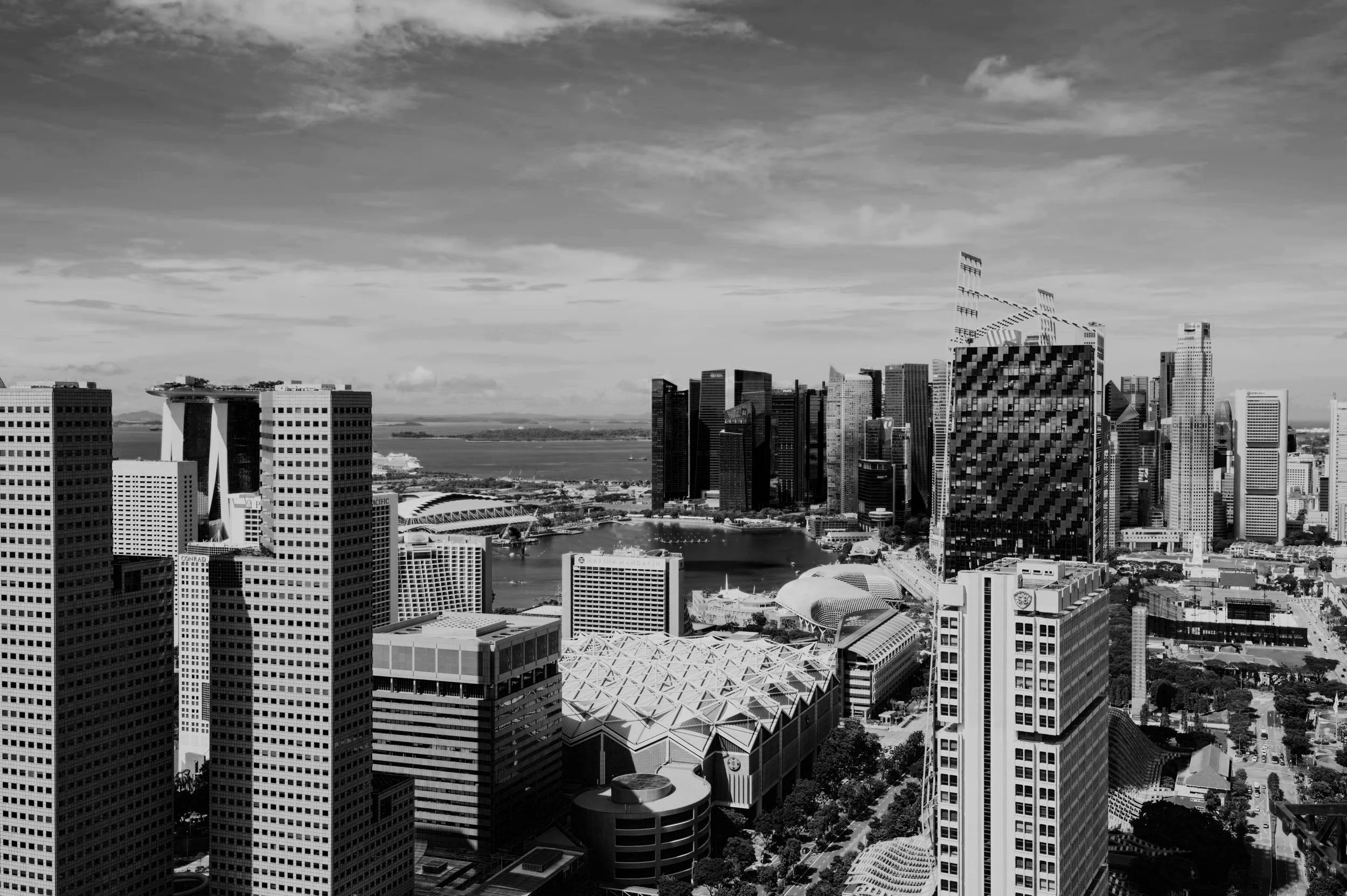Black and white aerial view of downtown San Francisco skyline with modern skyscrapers, the Embarcadero, and Bay Bridge in the distance.