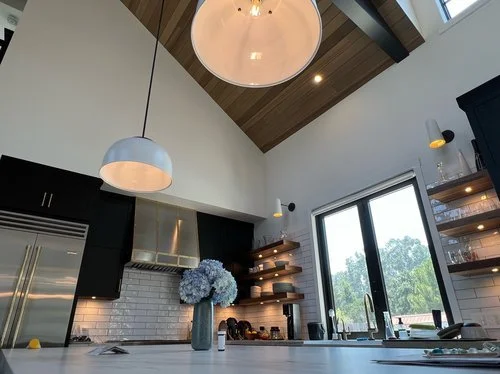 Modern kitchen with pendant lights, open shelving, and a window showing trees outside.