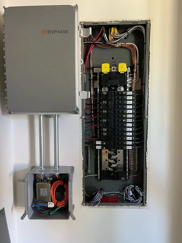 Electrical panel with multiple circuit breakers and wiring, and an accompanying remote enclosure mounted on the wall.